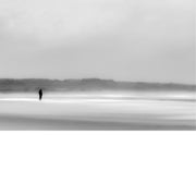 Kleine silhouet van een wandelaar op het wijde, nevelige strand van Wissant, waar zand, zee en lucht in zachte grijstinten in elkaar overlopen.