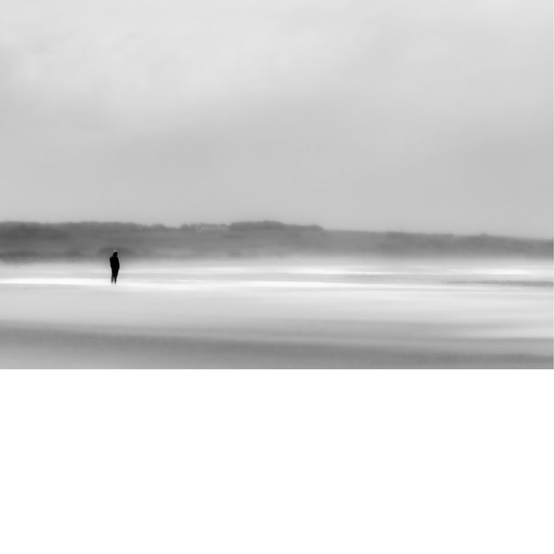 Kleine silhouet van een wandelaar op het wijde, nevelige strand van Wissant, waar zand, zee en lucht in zachte grijstinten in elkaar overlopen.