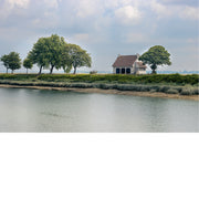 Wit huisje met rood dak tussen weelderige bomen op een groene oever in Honfleur, weerspiegeld in kalm water onder een bewolkte lucht.