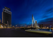 Erasmusbrug en verlichte hoogbouw met het opschrift R'DAM in het diepblauwe avondlicht, met strepen van bewegende wolken.