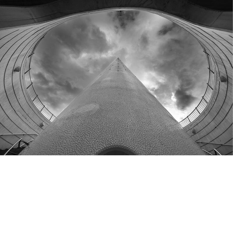 Blik omhoog door een ronde opening in de witte architectuur van de Ciutat de les Arts i les Ciències in Valencia, met een puntige constructie tegen een dramatische wolkenlucht.