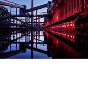 Cokesfabriek van Zollverein in Essen met rood verlichte gevel en stalen transportbanden, weerspiegeld in een waterbekken tijdens het blauwe uur.