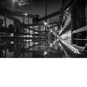 Stalen leidingen, transportbanden en een hoge schoorsteen van Zollverein in Essen weerspiegelen 's nachts in stil water.