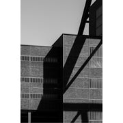 Bakstenen gevel met lange rijen vensters van Zollverein in Essen, doorsneden door de scherpe schaduw van een stalen constructie.