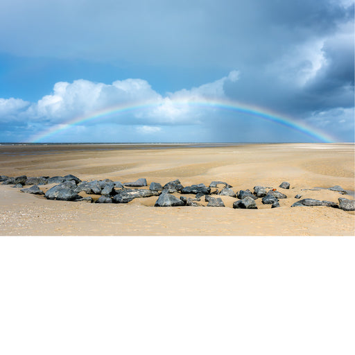 Een regenboog welft zich over het strand en de zee na een regenbui.
