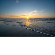 Een weids uitzicht over de zee tijdens zonsondergang. De zachte golven rollen over het natte zand en reflecteren de gouden lucht.