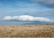 Een dramatisch landschap met een uitgestrekt, dor grasveld onder een blauwe lucht die gedomineerd wordt door één opvallende, langgerekte wolk.