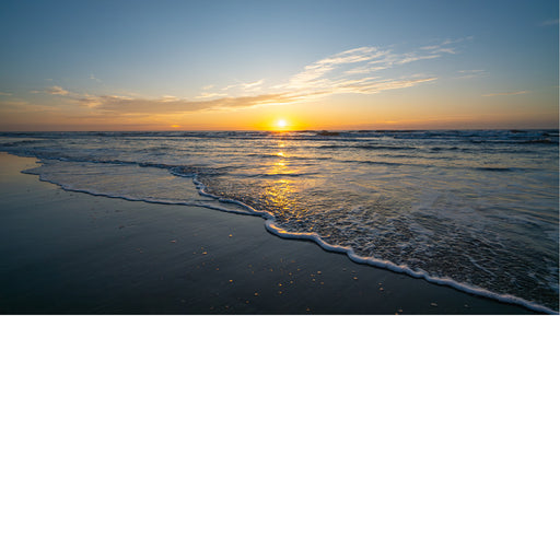 Een prachtige zonsondergang waarbij de zon precies op de horizon rust. De warme stralen weerspiegelen op het natte zand en het schuim van de zachte golven.