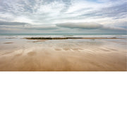 Een weids panorama van een breed strand bij eb. Een opvallende, langgerekte wolk domineert de horizon boven de rustige zee.