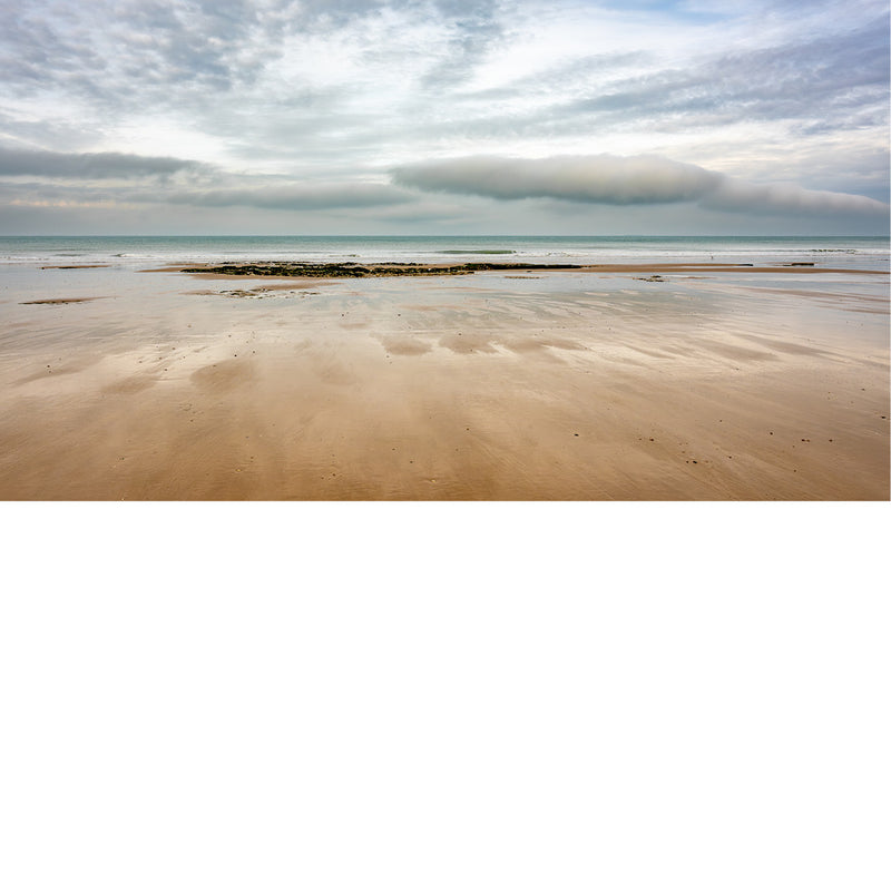 Een weids panorama van een breed strand bij eb. Een opvallende, langgerekte wolk domineert de horizon boven de rustige zee.