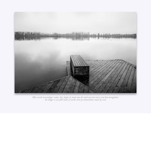 Een melancholisch landschap in zwart-wit. Een houten steiger strekt zich uit in kalm, spiegelglad water, omhuld door lichte mist op de achtergrond.