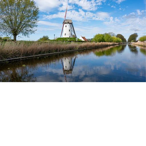 Een klassiek Hollands of Vlaams polderlandschap waarbij een grote witte windmolen perfect en stil wordt weerspiegeld in het water van een kaarsrecht kanaal.