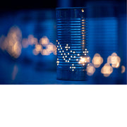 Geperforeerd blikje met een kaars erin werpt een sterrenpatroon van lichtpuntjes, omgeven door een wazige avondsfeer met warme bokehlichtjes.