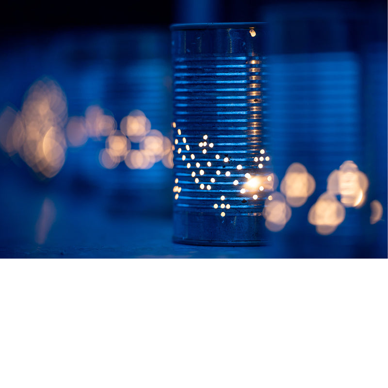 Geperforeerd blikje met een kaars erin werpt een sterrenpatroon van lichtpuntjes, omgeven door een wazige avondsfeer met warme bokehlichtjes.