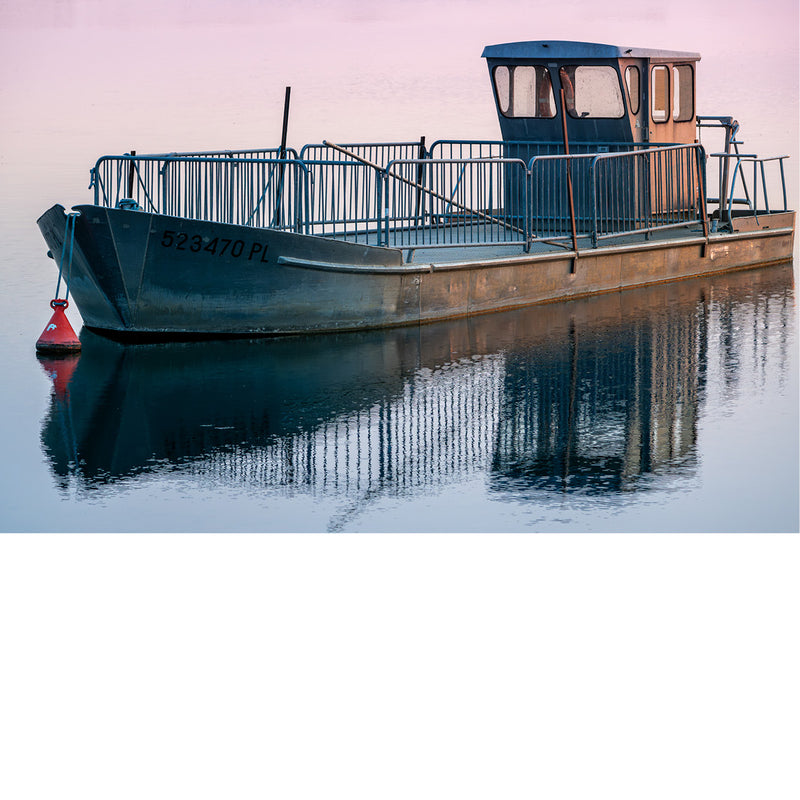 Close-up van een aangemeerde, verweerde boot met stalen reling, cabine en registratienummer, weerspiegeld in roze getint water.
