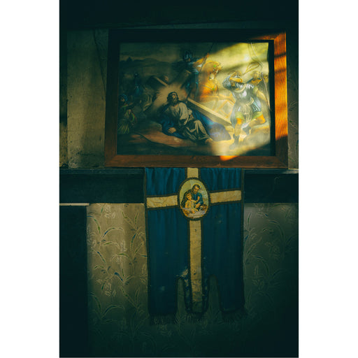 Verlaten huis met achtergebleven religieuze voorwerpen. Het zonlicht speelt op het geweldadige tafereel terwijl Jezus  zijn kruis draagt. Het vredige rust in de schaduw. Aanklacht tegen geweld 