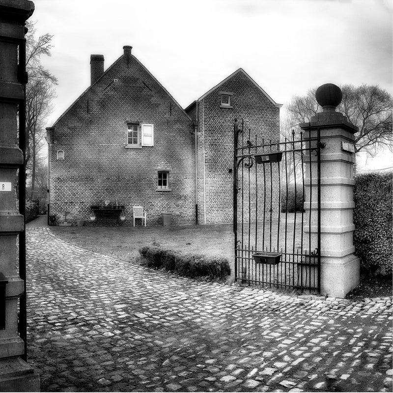 Zwart-wit foto van een historisch huis met grote inrijpoort en smeedijzeren poort. Erfgoed 