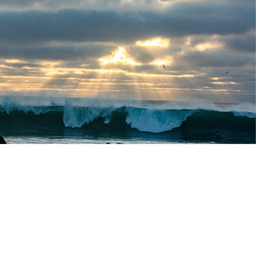 Een ontstuimige zee waar de zon door de wolken straalt.