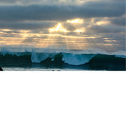 Een ontstuimige zee waar de zon door de wolken straalt.