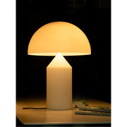 Gloeiende paddenstoelvormige tafellamp verlicht een donker interieur, met een notitieboekje en een opgevouwen tijdschrift binnen handbereik op tafel.