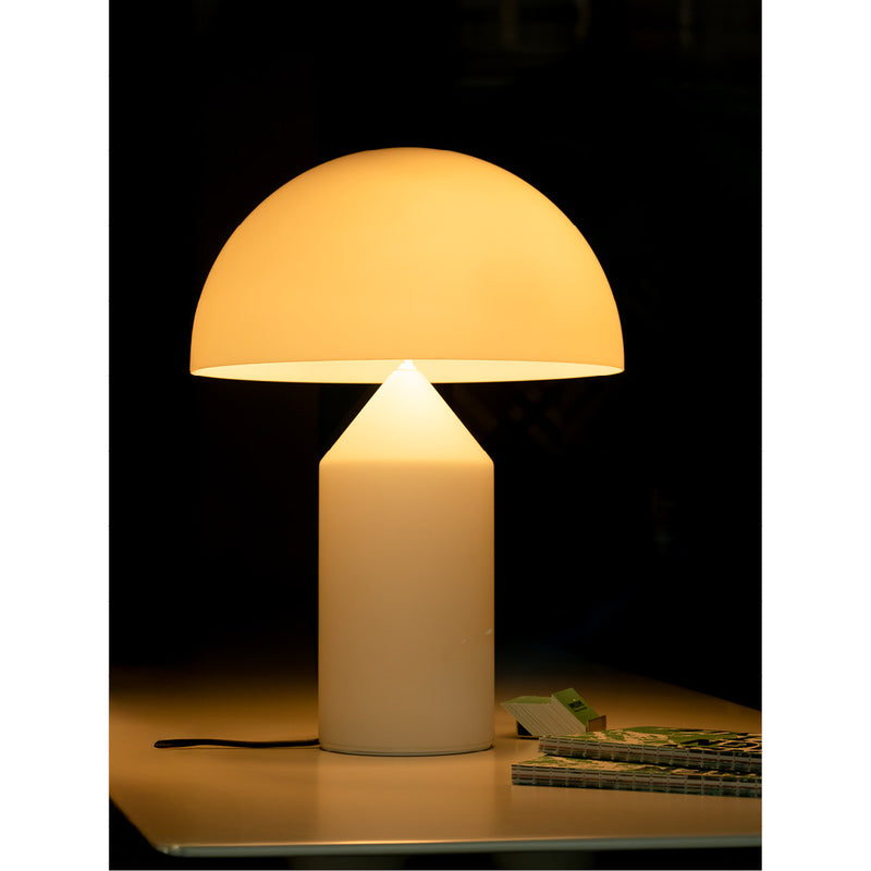 Gloeiende paddenstoelvormige tafellamp verlicht een donker interieur, met een notitieboekje en een opgevouwen tijdschrift binnen handbereik op tafel.