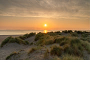 Zon komt op boven de zee bij Texel, met duingras en zandduinen op de voorgrond en een wolkenlucht in warme tinten.