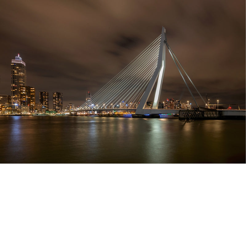 Erasmusbrug en de verlichte skyline van Rotterdam weerspiegelen in het water tijdens een lange nachtopname.