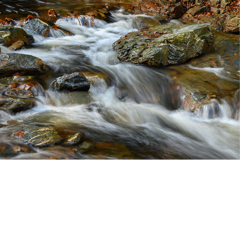 Water stroomt met kracht tussen donkere, met mos begroeide rotsblokken door een beek, met een wazig, gladgetrokken watereffect.