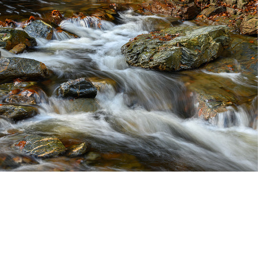 Water stroomt met kracht tussen donkere, met mos begroeide rotsblokken door een beek, met een wazig, gladgetrokken watereffect.