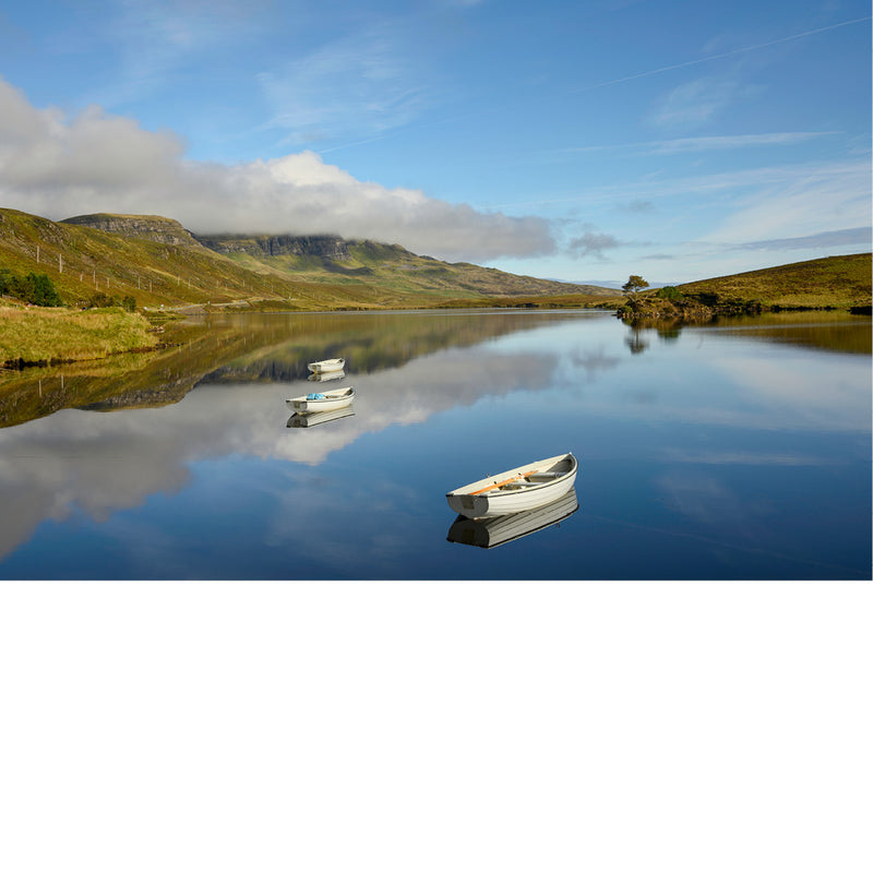 Drie kleine roeibootjes drijven verspreid op een spiegelglad meer op het eiland Skye, met glooiende heuvels en wolken die weerspiegelen in het water.
