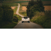 Een oldtimer rijdt over een lange landelijke weg in West-Vlaanderen, met uitzicht op een uitgestrekt landschap. Rust en genieten komen samen in het beeld. De uitgestrektheid van de omgeving brengt ruimte en zuurstof in elk interieur.