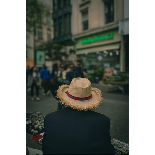 Een oude straatverkoper langs een straat in het drukke Parijs. Van onder zijn strohoed lacht hij de voorbijgangers minzaam toe. Ze vormen mee het decor, hij is de enige vaste waarde in dit beeld. Deze foto nam ik in de levendige wijk 'Le Marais'.