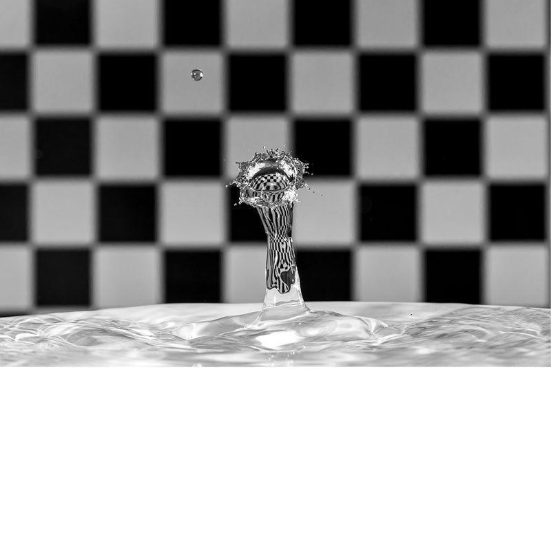 macro-opname van een waterdruppel op het moment van impact met reflectie in druppel van zwart met wit geblokte achtergrond