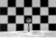 macro-opname van een waterdruppel op het moment van impact met reflectie in druppel van zwart met wit geblokte achtergrond