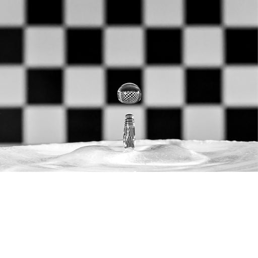 macro-opname van een waterdruppel op het moment van impact met reflectie in druppel van zwart met wit geblokte achtergrond