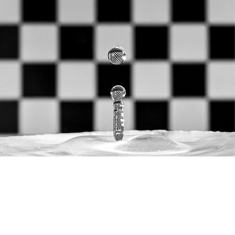 macro-opname van een waterdruppel op het moment van impact met reflectie in druppel van zwart met wit geblokte achtergrond