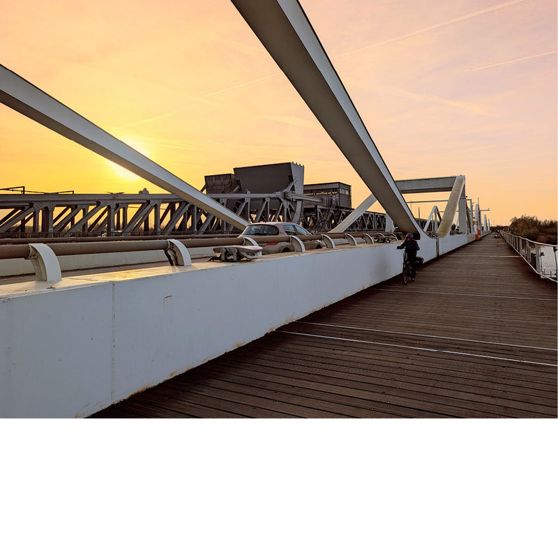 Een fietser kruist een auto op de Temsebrug in de ochtend, tijdens de zonsopgang. 