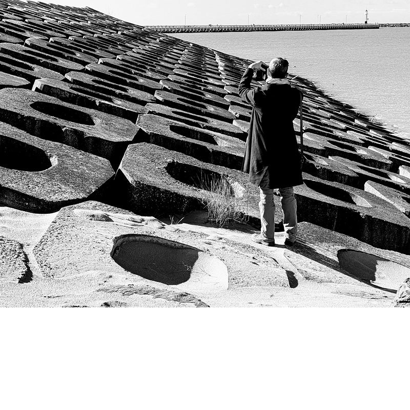 Foto van een man die een foto maakt van de Pier van Oostende, staand op golfbrekers.
