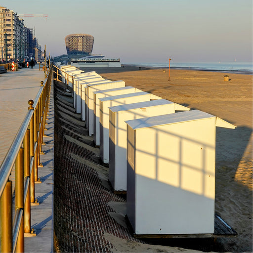 De opkomende zon werpt schaduwlijnen op de strandcabines, het casino van Middelkerke op de achtergrond.