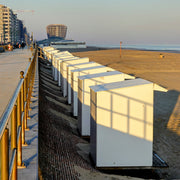 De opkomende zon werpt schaduwlijnen op de strandcabines, het casino van Middelkerke op de achtergrond.