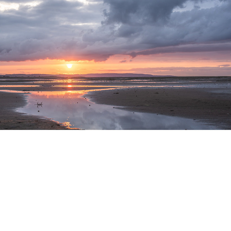 Deze zonsondergang is fantastisch. Een warme gloed met daarboven intense wolken en onderaan reflecties op het strand.