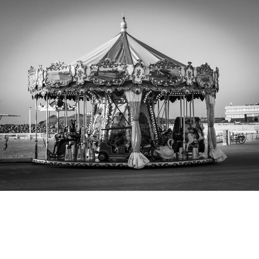 Draaimolen met paardjes, een zwaan en een oldtimer op de zeedijk van Oostende, met sierlijke panelen en lampjes onder een puntdak.
