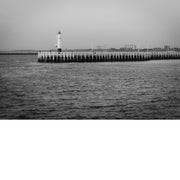 Houten pier in Oostende met een klein wit vuurtorentje aan het uiteinde, met duinen en appartementsgebouwen aan de horizon.