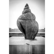 Monumentaal beeld van een wulkschelp op een betonnen sokkel op de pier van Oostende, met een ruwe, verweerde structuur.