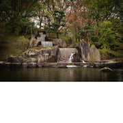 Trapsgewijze waterval tussen grote rotsblokken en gesnoeide dennen, die uitkomt in een stille vijver in de Japanse tuin van Hasselt.