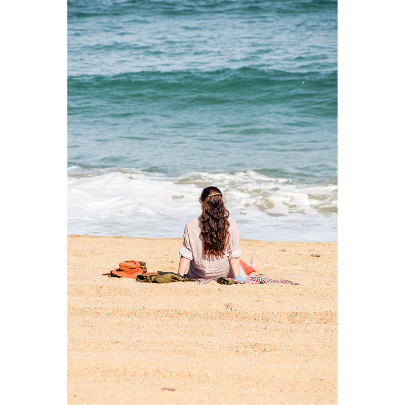 Een vrouw zit op een dekentje op het strand en kijkt naar de zee