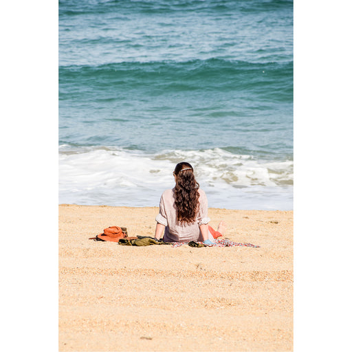 Een vrouw zit op een dekentje op het strand en kijkt naar de zee