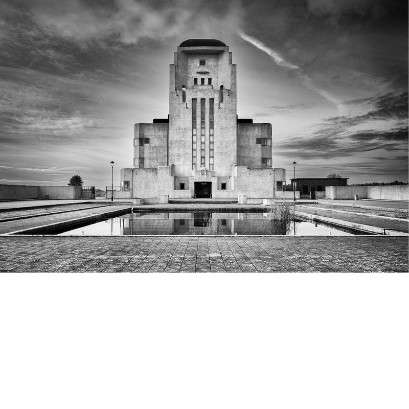 Het monumentale zendgebouw van Radio Kootwijk rijst symmetrisch op uit het Veluwse zand en spiegelt in de vijver ervoor.