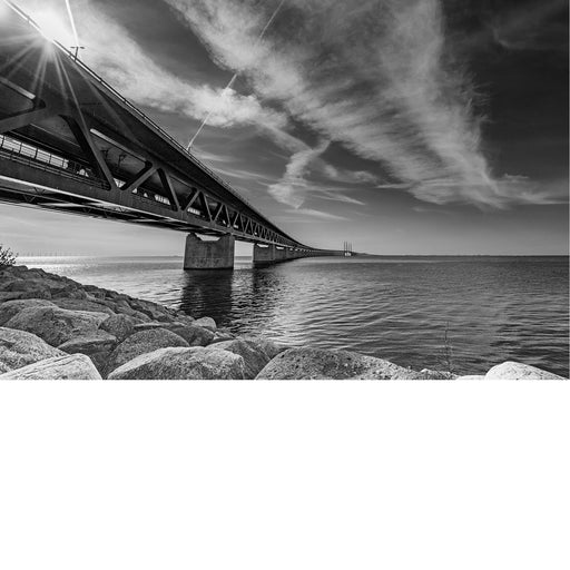 Öresundbrug strekt zich vanaf de rotsige oever tot ver over het water uit, met de zon die tussen de constructie door breekt.