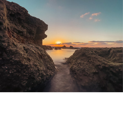 Een zonsondergang bij de kust, met een ruige kustlijn en panoramisch uitzicht. 